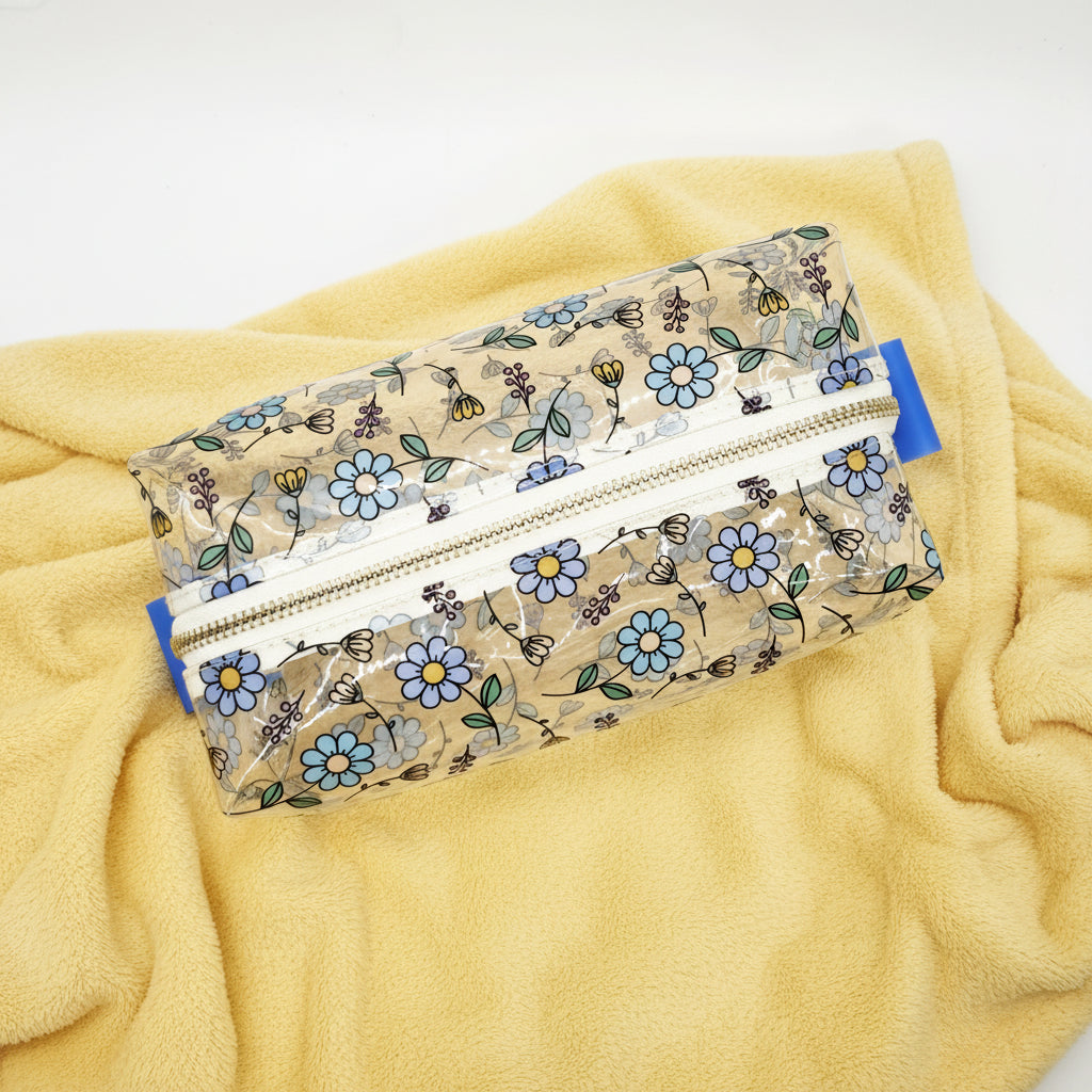 A clear zippered pouch with a white floral print featuring blue flowers, green leaves, and small bees, shown on a plain white background.